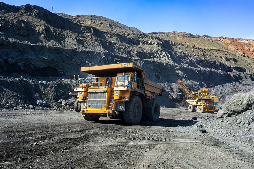 Two yellow dumb trucks are seen operating at a mining site.