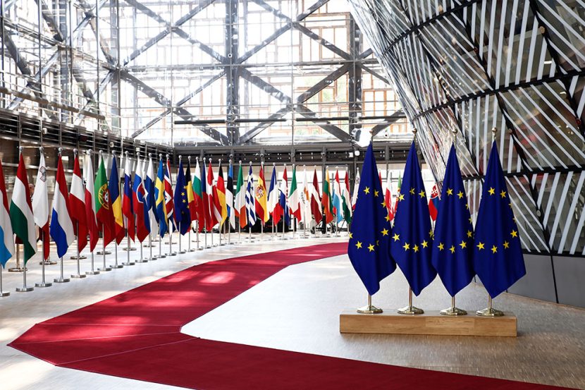 European Union country flags stand inside a brightly lit building.