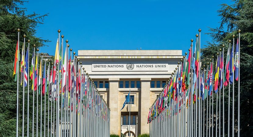 Country flags fly outside the United Nations building under a clear blue sky.